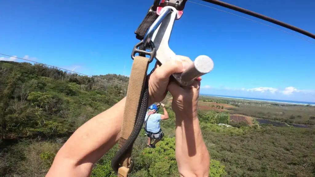 Zipline POV with hands gripping the bar and Oahu coastline in the distance